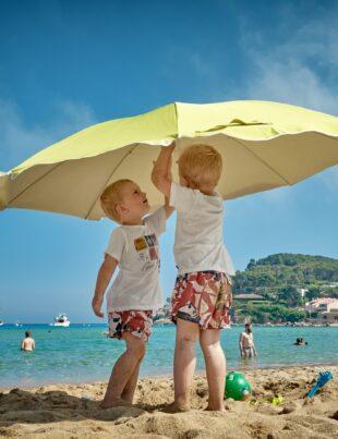 two children playing under umbrella on seashore